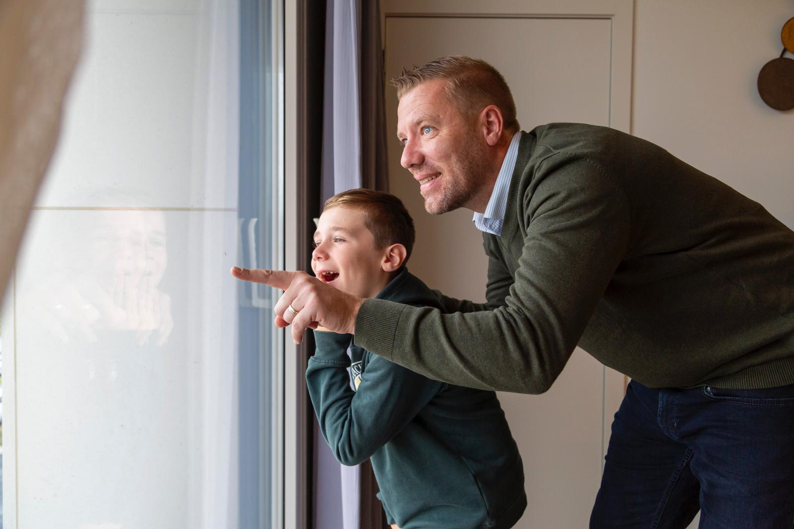 Vader en zoon kijken uit het raam van hun unit